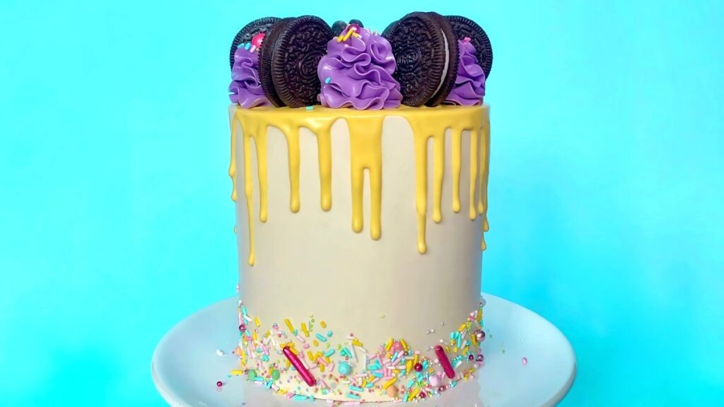 decorated Oreo Funfetti cake, covered in vanilla buttercream, a yellow white chocolate drip, colorful sprinkles, and Oreo cookis