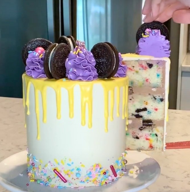 Cutting into the Oreo Funfetti cake to show the inside filled with Oreos and sprinkles perfect as a birthday cake recipe