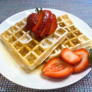 homemade waffles served on a plate with maple syrup, powdered sugar, and fresh strawberries