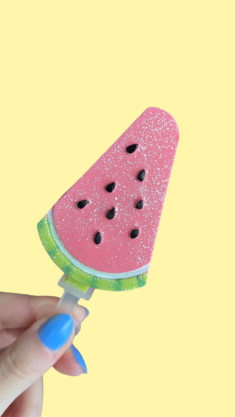 Fingers holding a watermelon caskicle in front of a yellow background