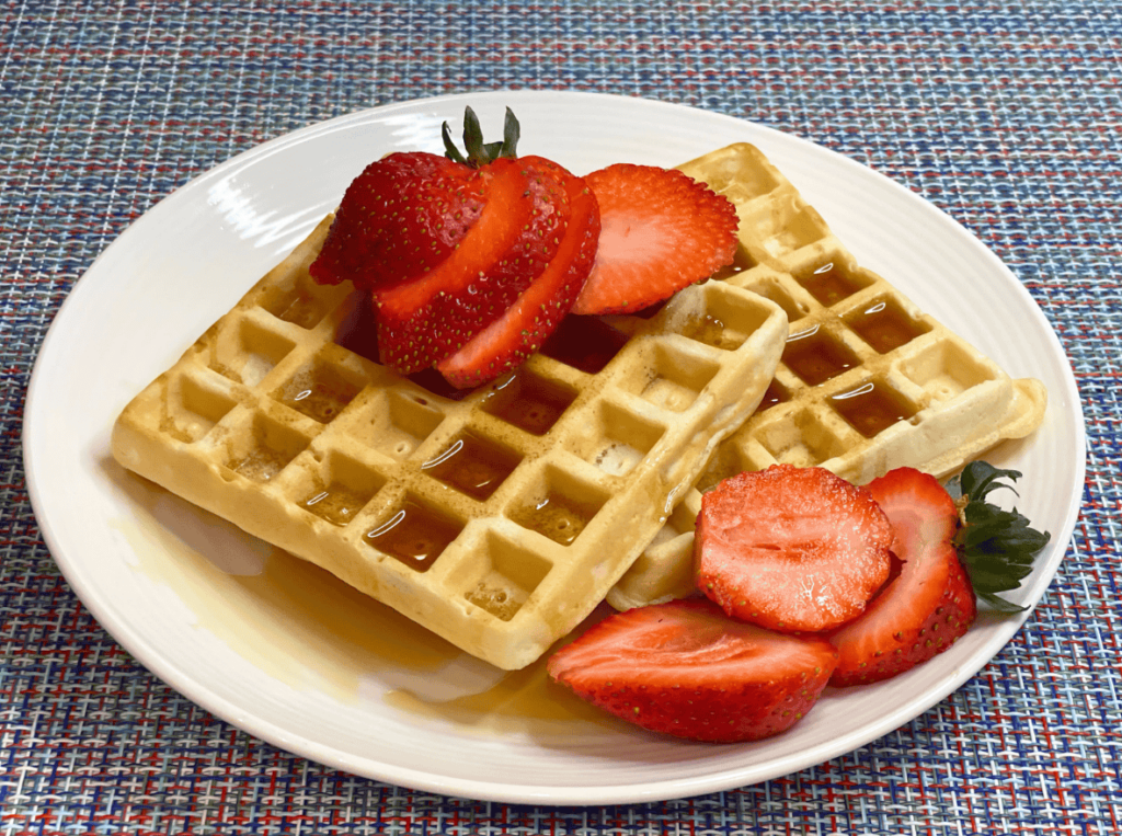 fresh homemade waffles served on a plate with maple syrup and fresh strawberries