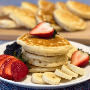 fluffy pancake on a plate topped with strawberries, bananas and bkueberries