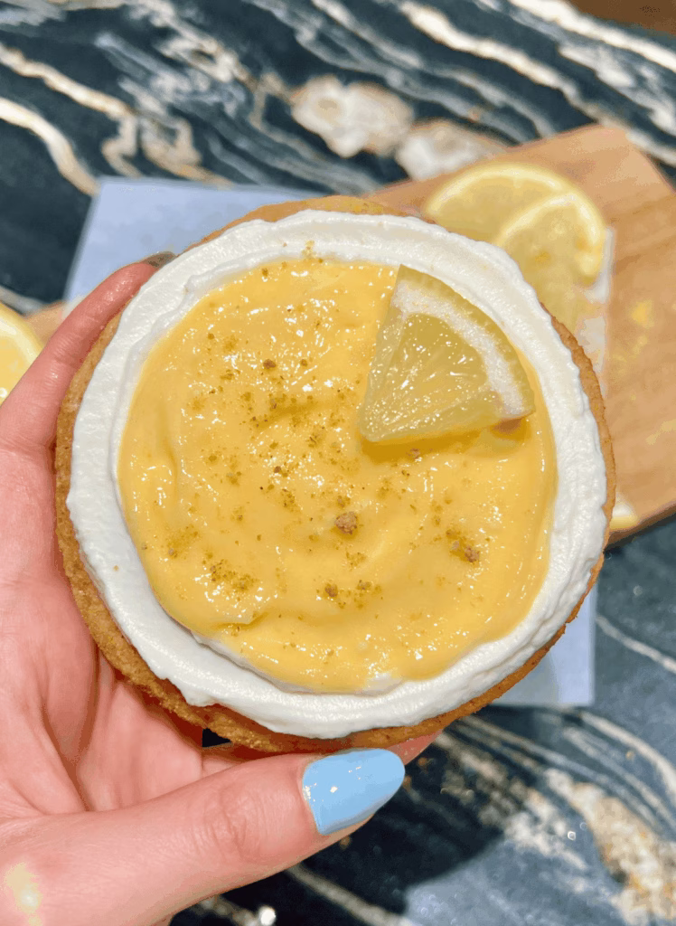 Close-up of a hand holding a full lemon cheesecake cookie