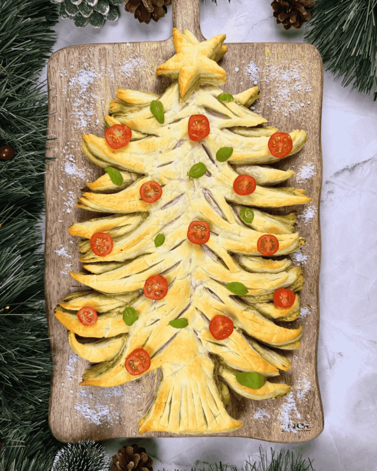 Baked puff pastry Christmas tree with green pesto filling on a wooden board.
