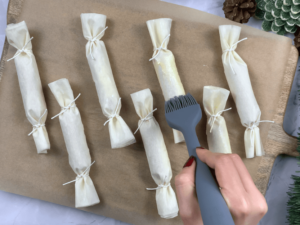 Unbaked phyllo hot dog crackers on a parchment lined tray being brushed with egg wash before baking.