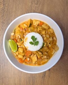 A close-up shot of a spoonful of chicken curry, showing the rich yellow sauce and a fresh lime wedge on the side of the plate.