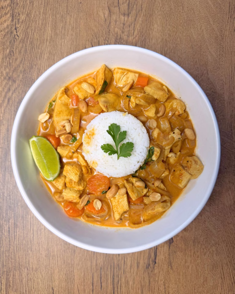A close-up shot of a spoonful of chicken curry, showing the rich yellow sauce and a fresh lime wedge on the side of the plate.