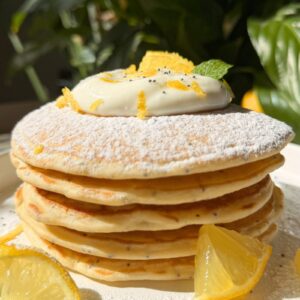 stacked lemon poppy seed pancake, showing the golden texture, poppy seed speckles, creamy yogurt topping.