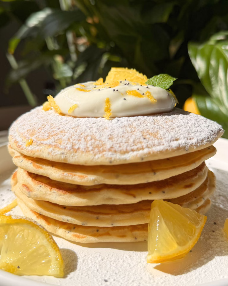 stacked lemon poppy seed pancake, showing the golden texture, poppy seed speckles, creamy yogurt topping.